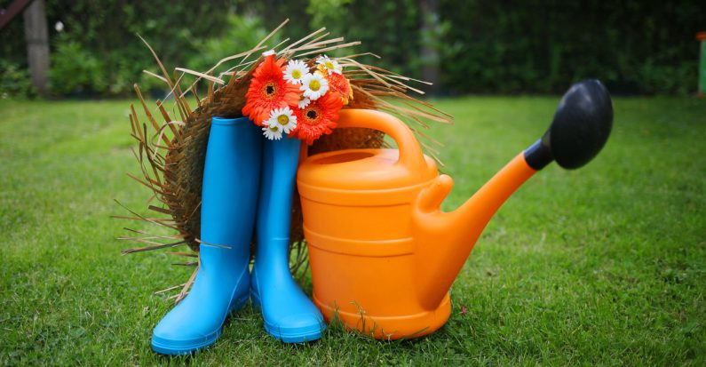 bottes en caoutchouc bleu arrosoir en plastique orange et chapeau de paille posés sur de la pelouse