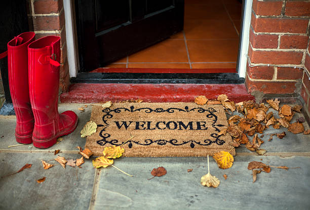 Paillasson welcome sur le perron d'une entrée décorée, avec bottes en caoutchouc rouges à côté