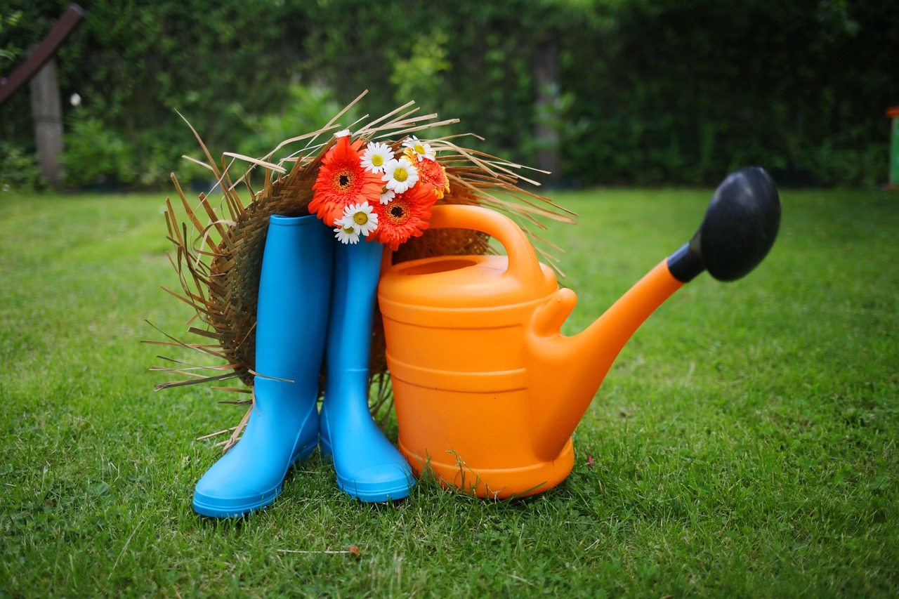 bottes en caoutchouc bleu arrosoir en plastique orange et chapeau de paille posés sur de la pelouse